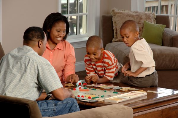 pai, mãe e dois filhos brincando com jogo de tabuleiro em volta de uma mesa